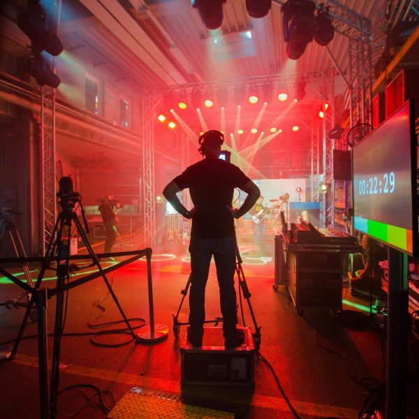 Imagefoto eines Technikers, der von den Effektlichtern einer Bühne beleuchtet wird, auf der eine Musikband spielt