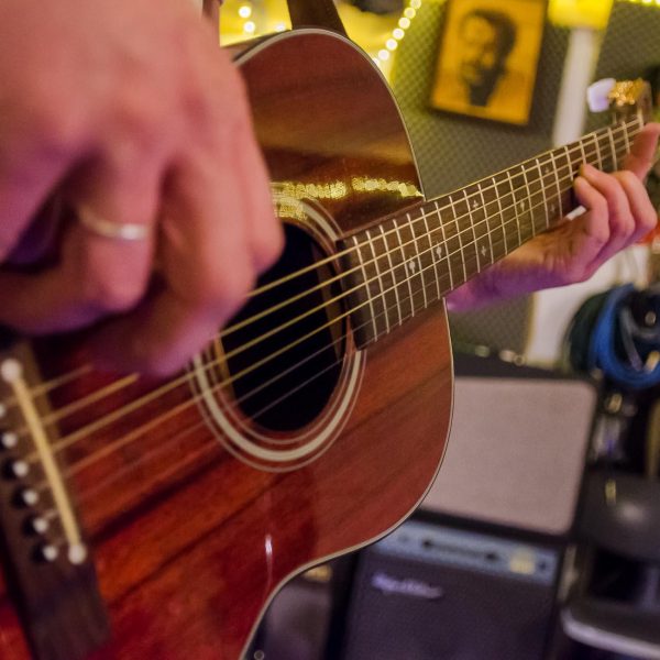 Imagefoto einer Akustikgitarre, die gespielt wird, wobei sich lediglich die Hand am Hals der Gitarre im Fokus befindet