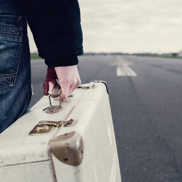 Imagefoto eines alten Reisekoffers, der von einer Person gehalten wird, die auf der Startbahn des Tempelhofer Flugfelds steht