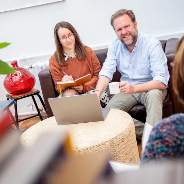 Corporate Fotografie in Berlin - Imagefoto eines Beratungsgesprächs zwischen zwei Geschäftsleuten, die auf einem Sofa sitzen, und einer dritten Person, die ihnen gegenüber sitzt